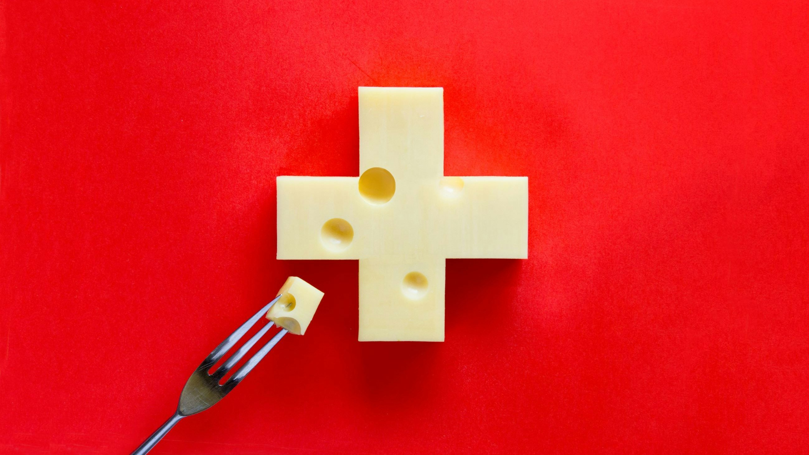 Swiss cross in form of cheese on red background, with a piece on fork