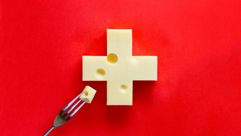 Swiss cross in form of cheese on red background, with a piece on fork