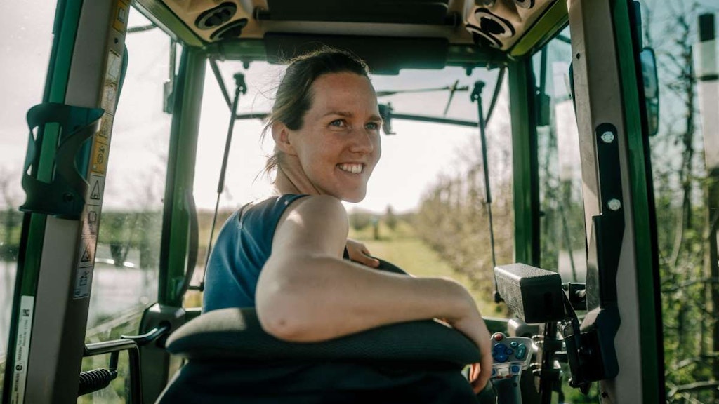 Junge Frau auf Traktor, blickt lächelnd zurück