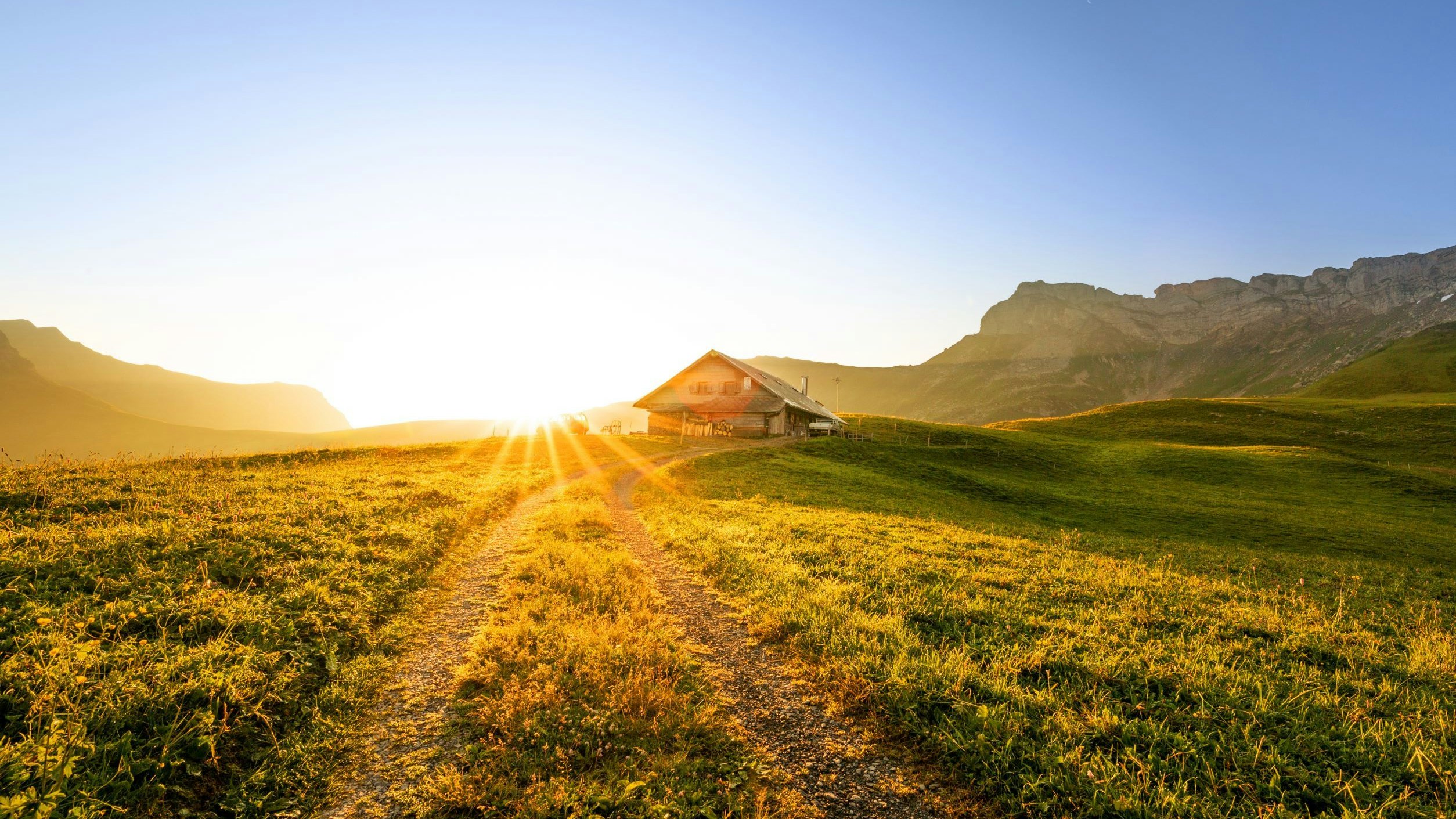 swiss chalet or farm in mountain landscape at sunrise with sunstar