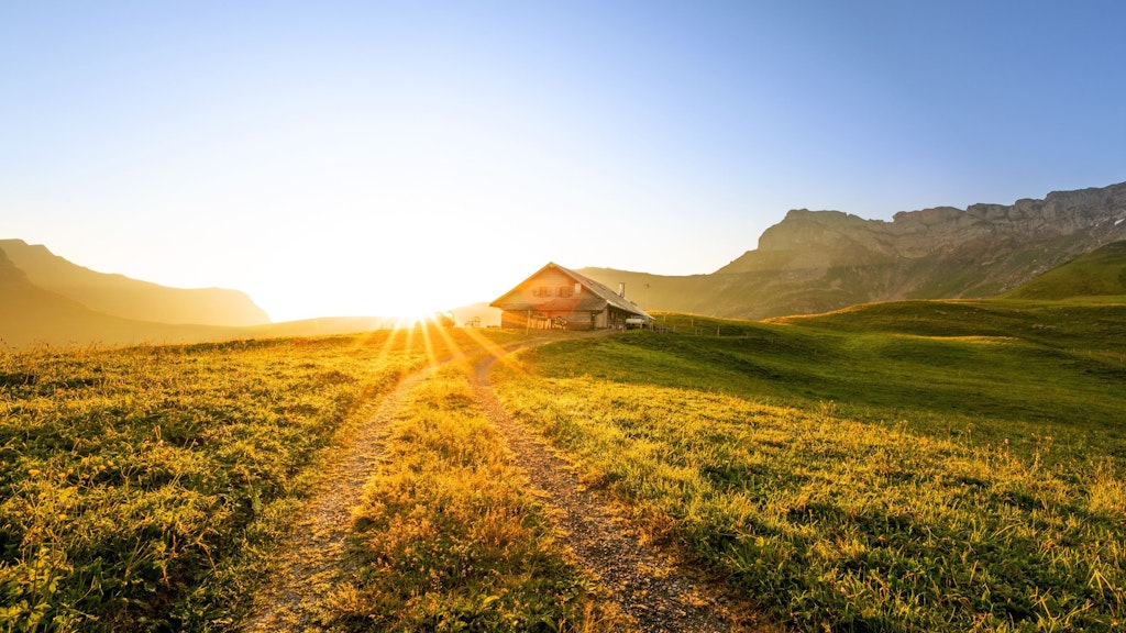 swiss chalet or farm in mountain landscape at sunrise with sunstar