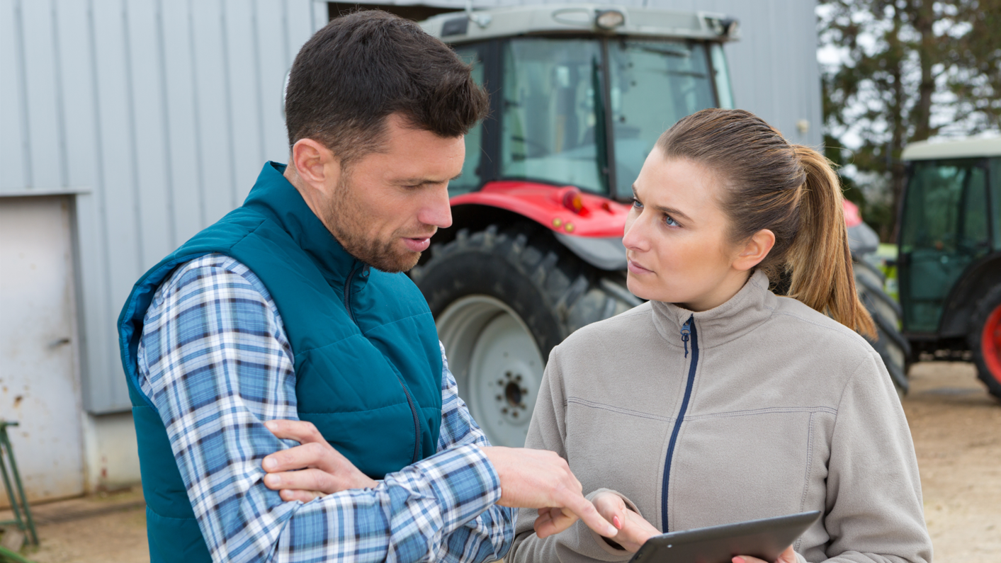 Ein Mann und eine Frau auf einem Landwirtschaftsbetrieb betrachten ein digitales Tablet.