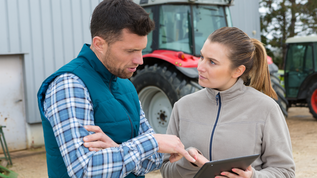 Ein Mann und eine Frau auf einem Landwirtschaftsbetrieb betrachten ein digitales Tablet.