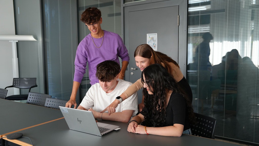 Vier Lernende die zusammen an einem Laptop arbeiten