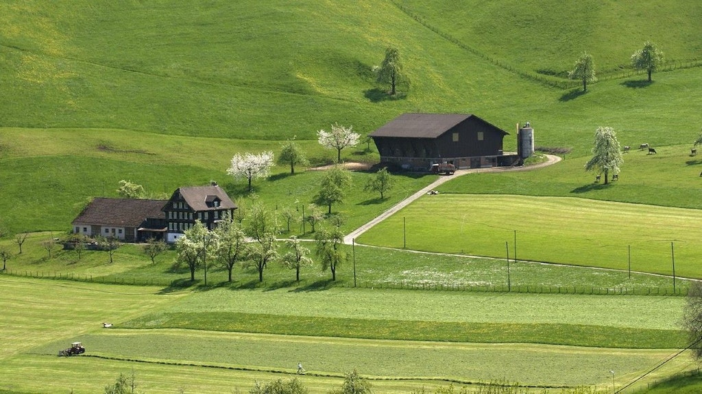 Zwei Bauernhöfe stehen inmitten hügeliger Felder an einem sonnigen Tag.