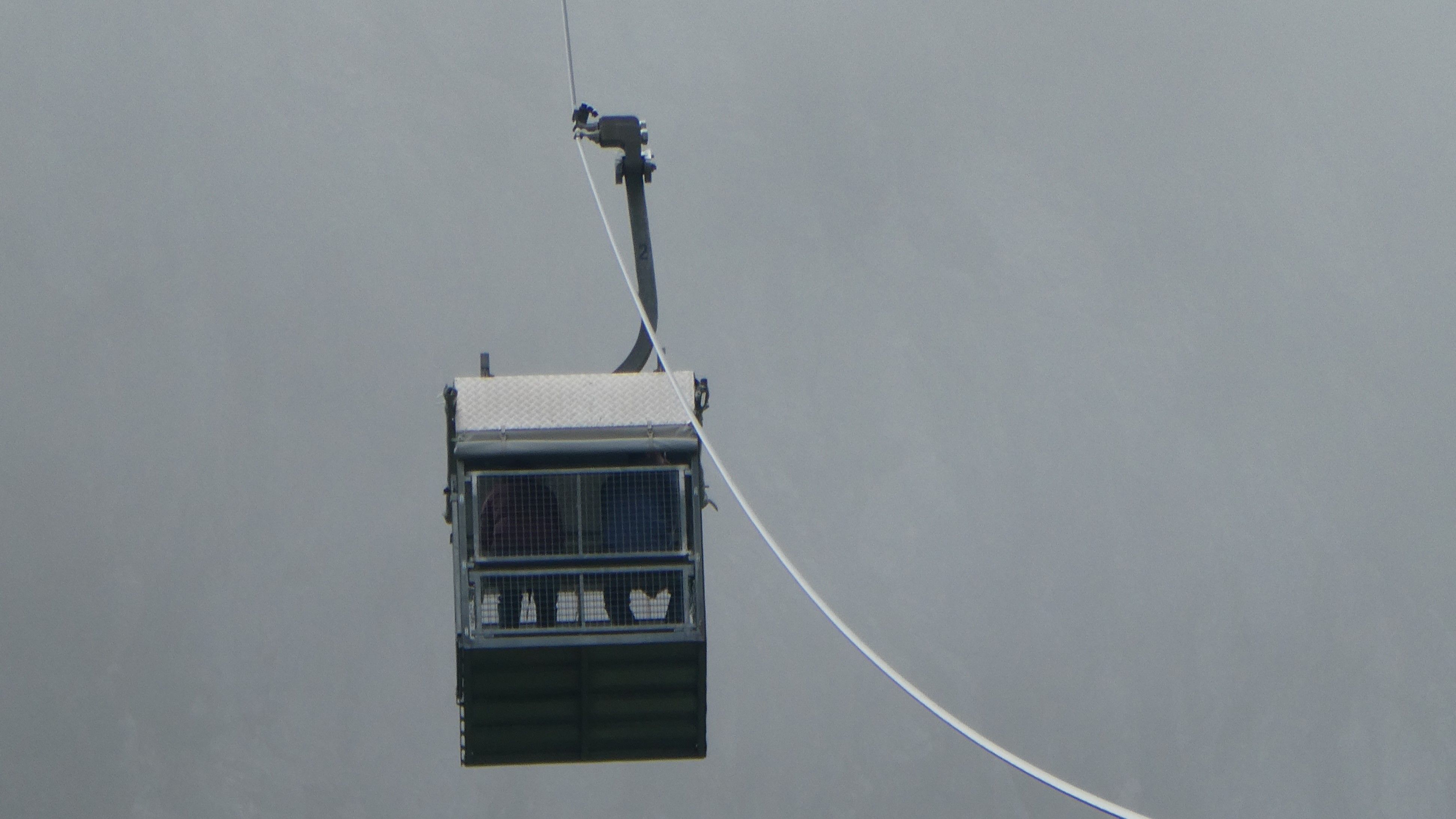 Geschlossene Kabine für zwei Personen an einem Seil im Nebel.