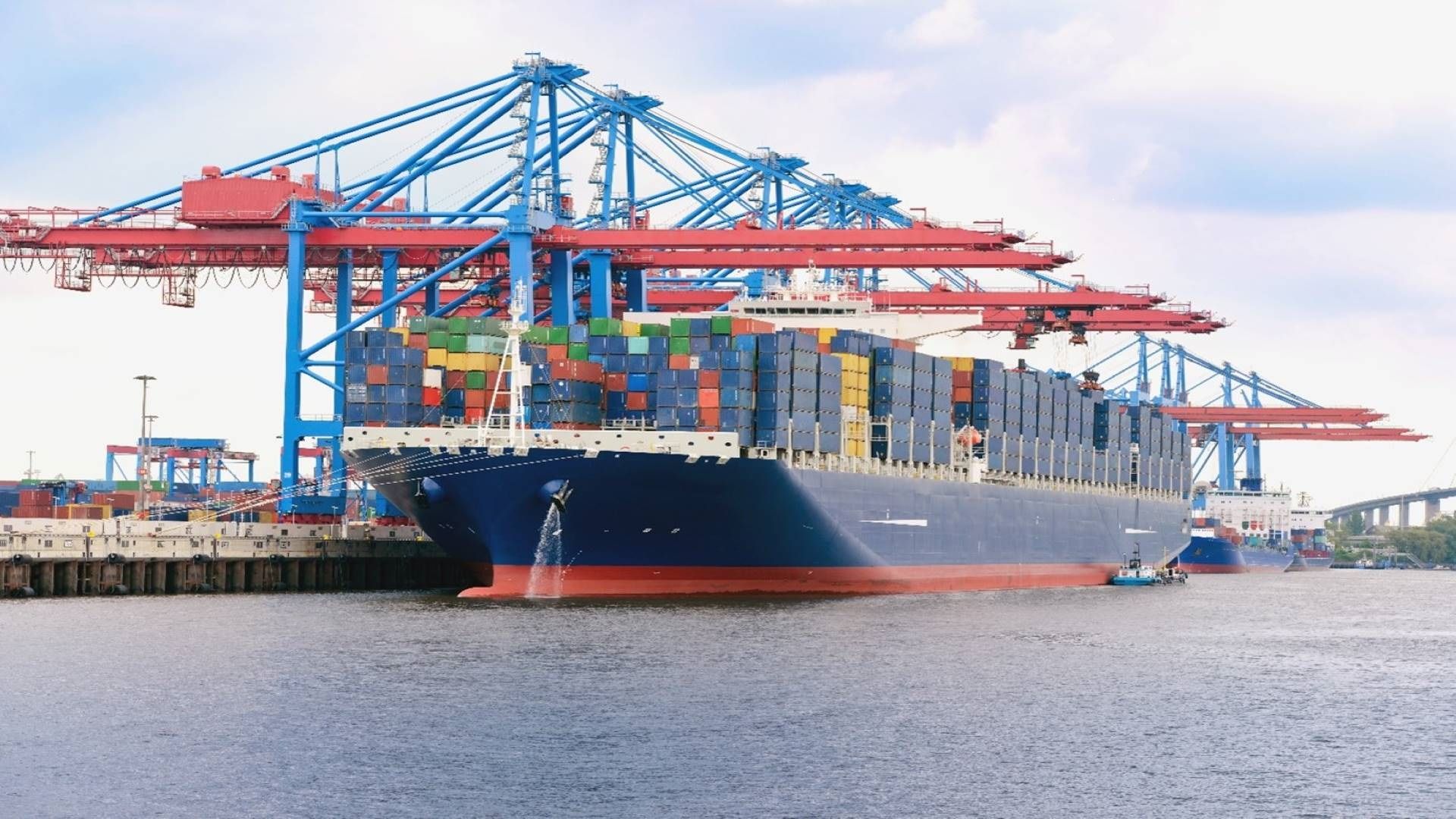 Ein Frachthafen mit einem grossen Cargoschiff, welches farbige Container transportiert.