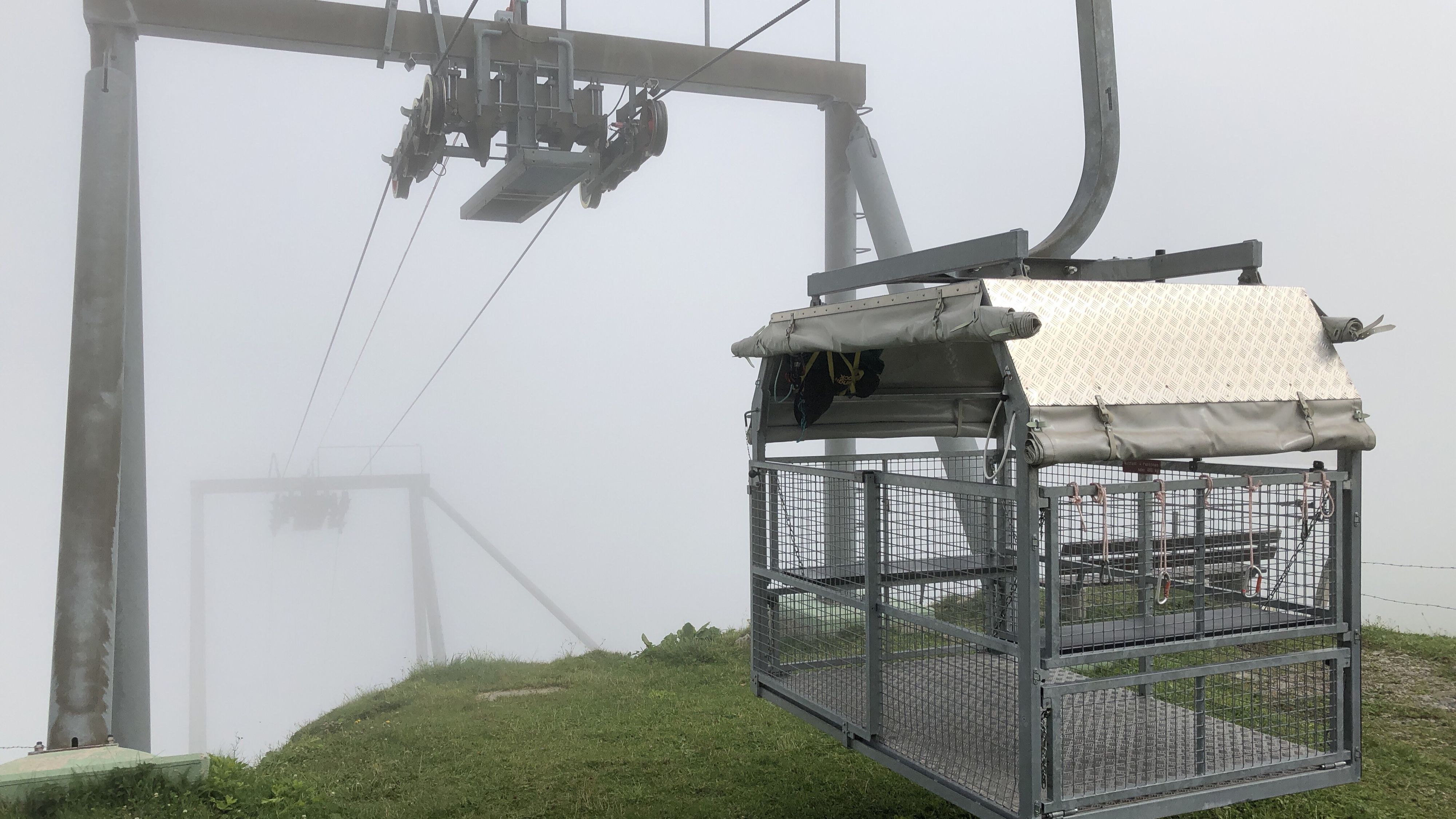 Personen- und Materialkabine mit Dach und Gitterwänden in der Nähe eines Pylons.