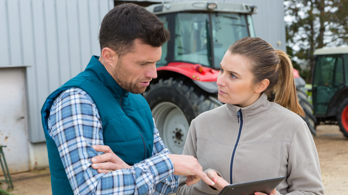 A man and a woman on a farm look at a tablet.