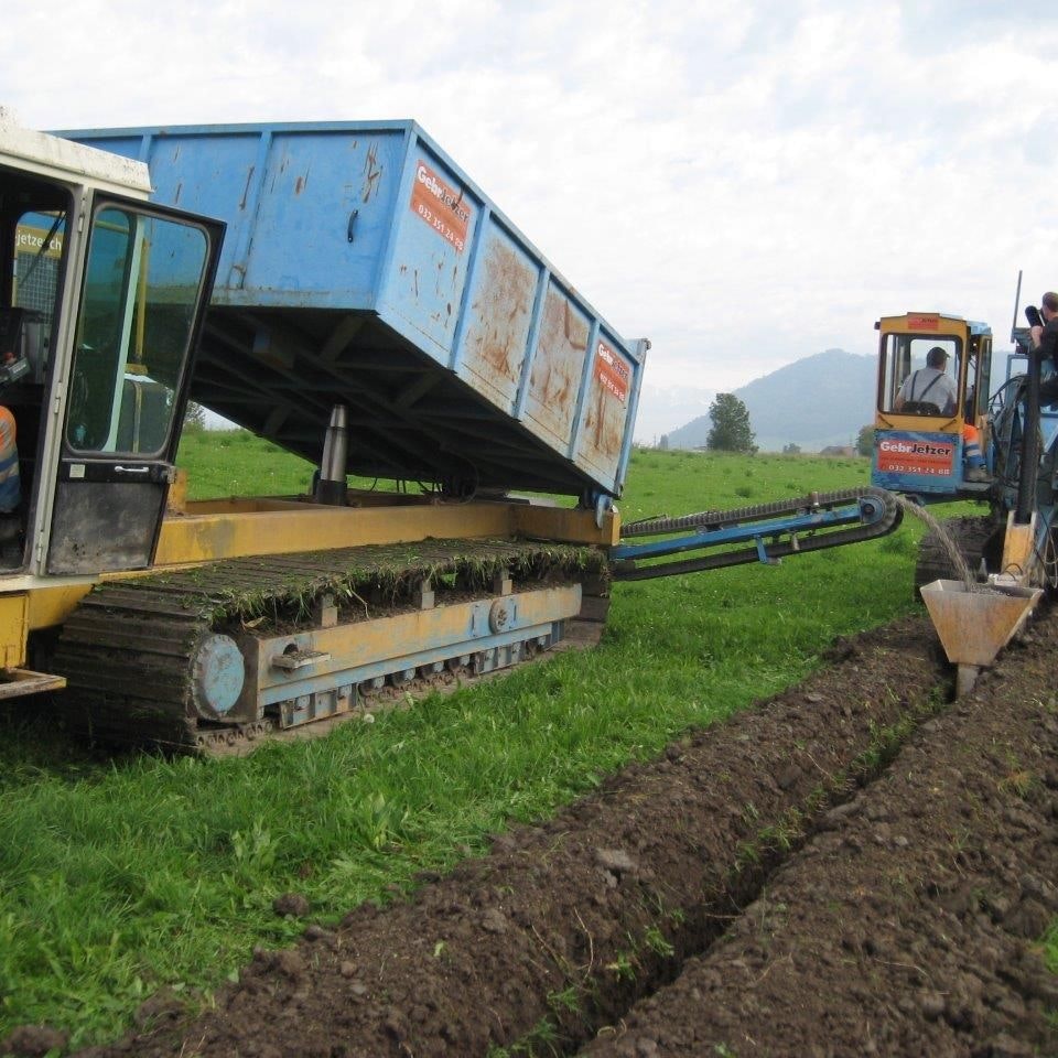 Un tracteur équipé d’une trancheuse et un véhicule à chenilles transportant du gravier installent une conduite de drainage dans une surface herbagère.