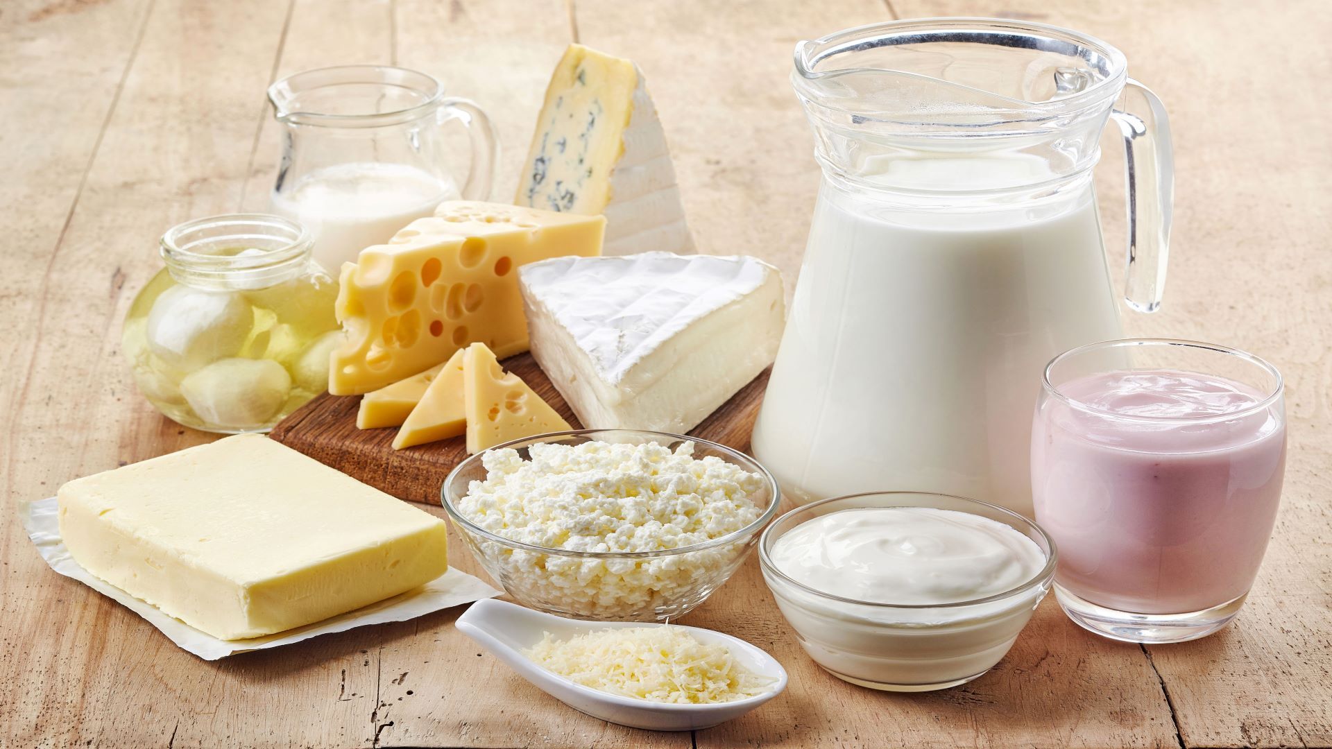 Sur une table en bois sont disposés un pot de lait, de la crème, une plaque de beurre, yogourts et différents morceaux de fromage.