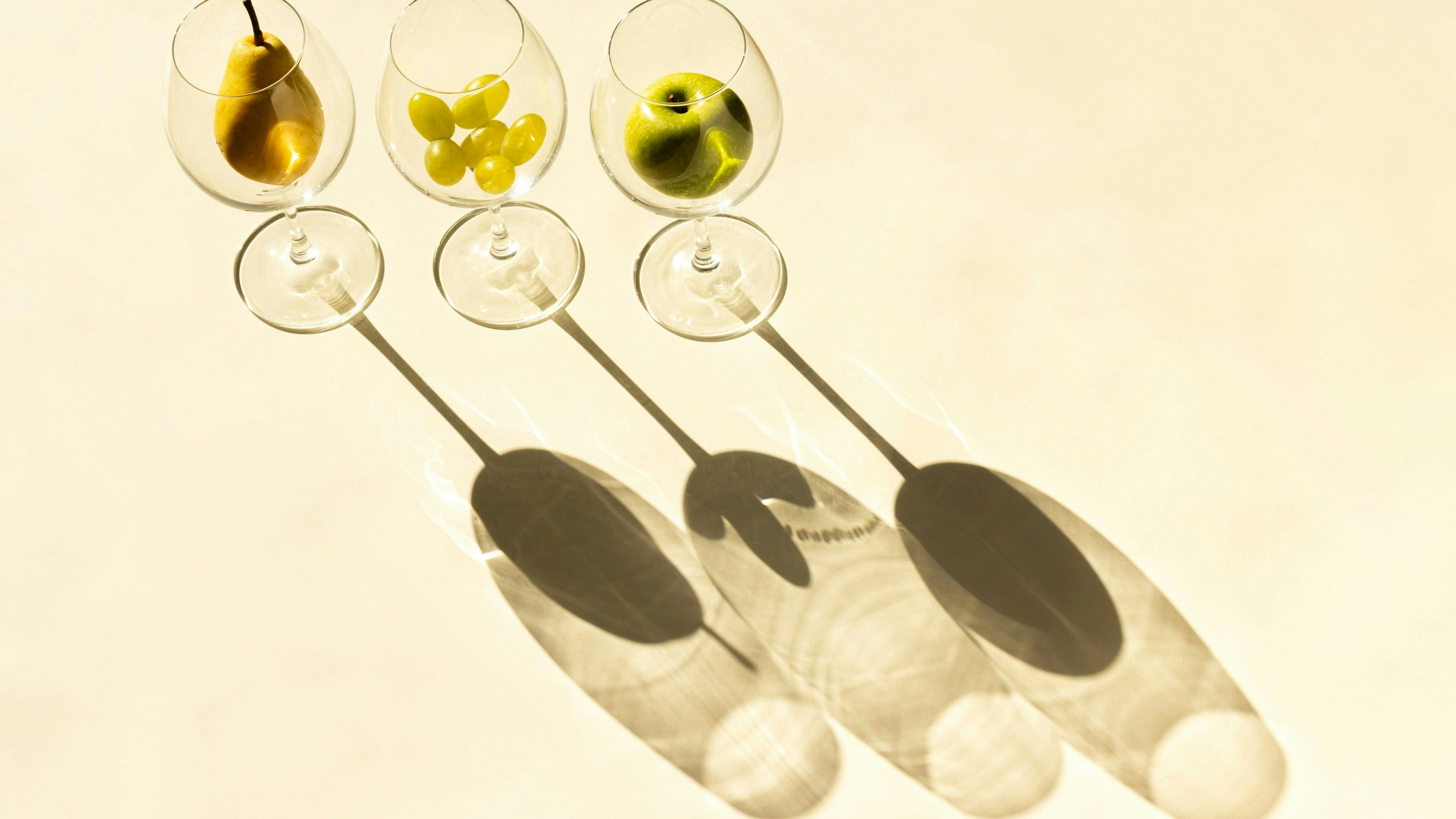 3 verres à vin avec poire, raisin et pomme et leur ombre projetée par la lumière