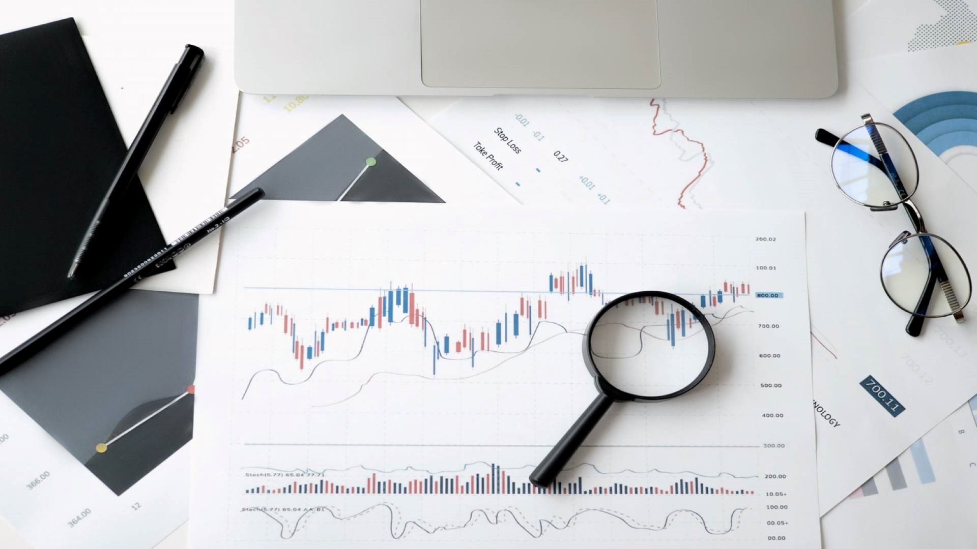 Des statistiques et des graphiques imprimés, une loupe, des lunettes et de quoi écrire sur une table.