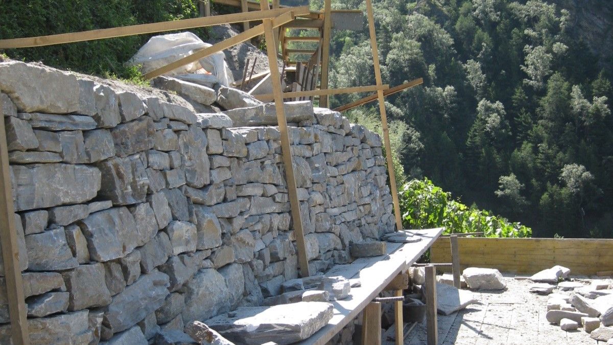 Mur de pierres sèches encore inachevé avec échafaudage sur une pente.