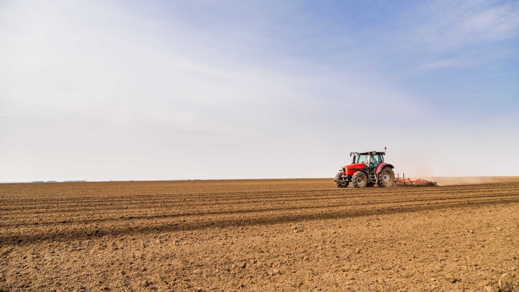Un agriculteur ou une agricultrice travaille au labourage d’un champs depuis son tracteur par un temps ensoleillé. 