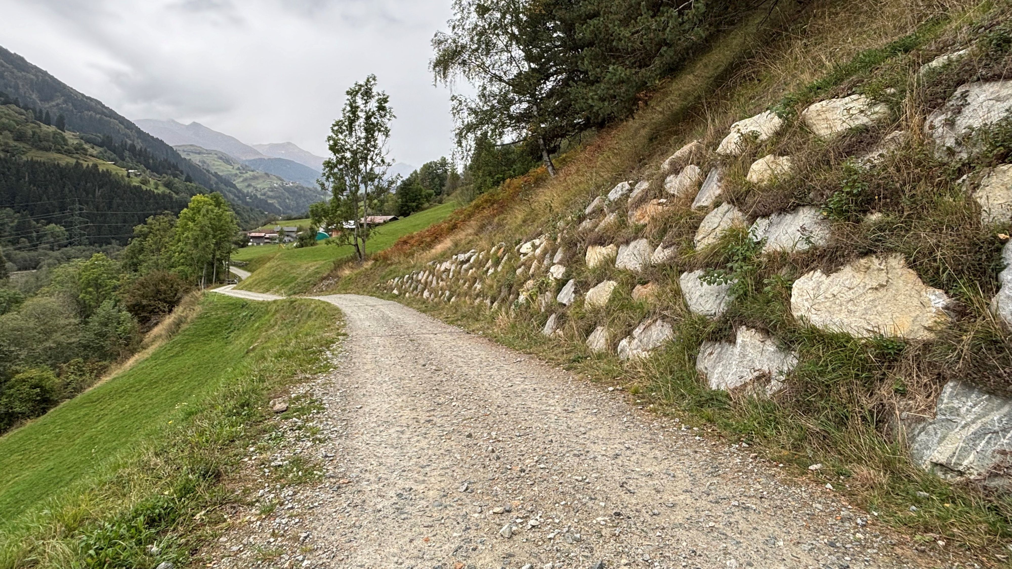 Le chemin gravelé est parallèle à la pente et est sécurisé par un talus sur le côté droit. Le talus est constitué de pierres naturelles, entre lesquelles pousse de l’herbe.