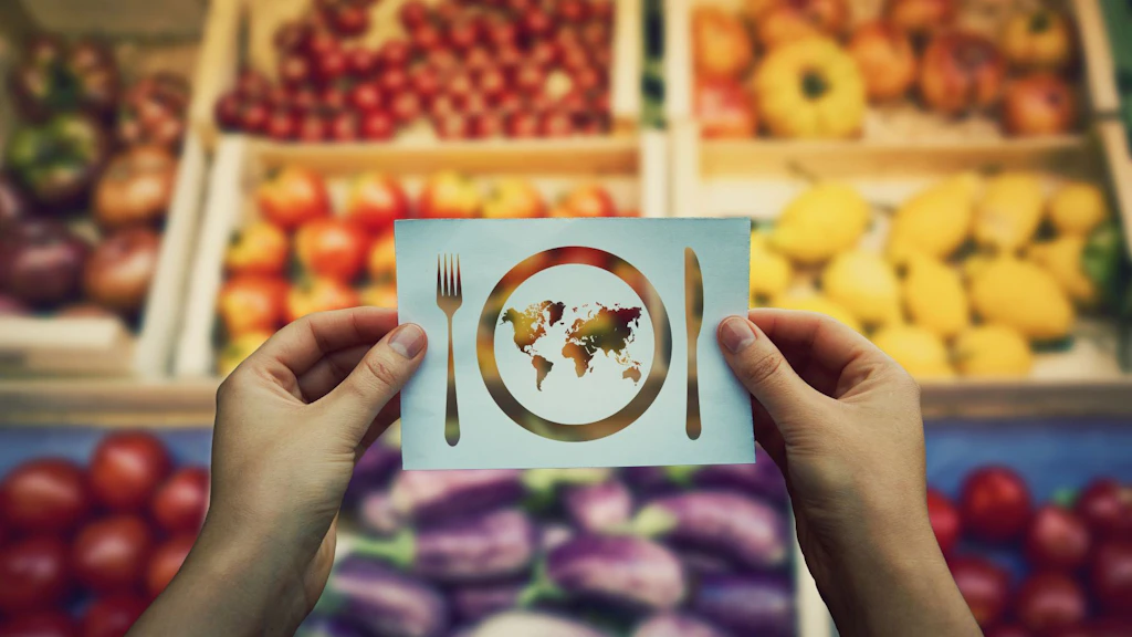 Des mains tiennent une feuille de papier avec une carte du monde dans une assiette avec le symbole du couteau et de la fourchette au-dessus des rayons du marché avec des légumes et des fruits en arrière-plan.