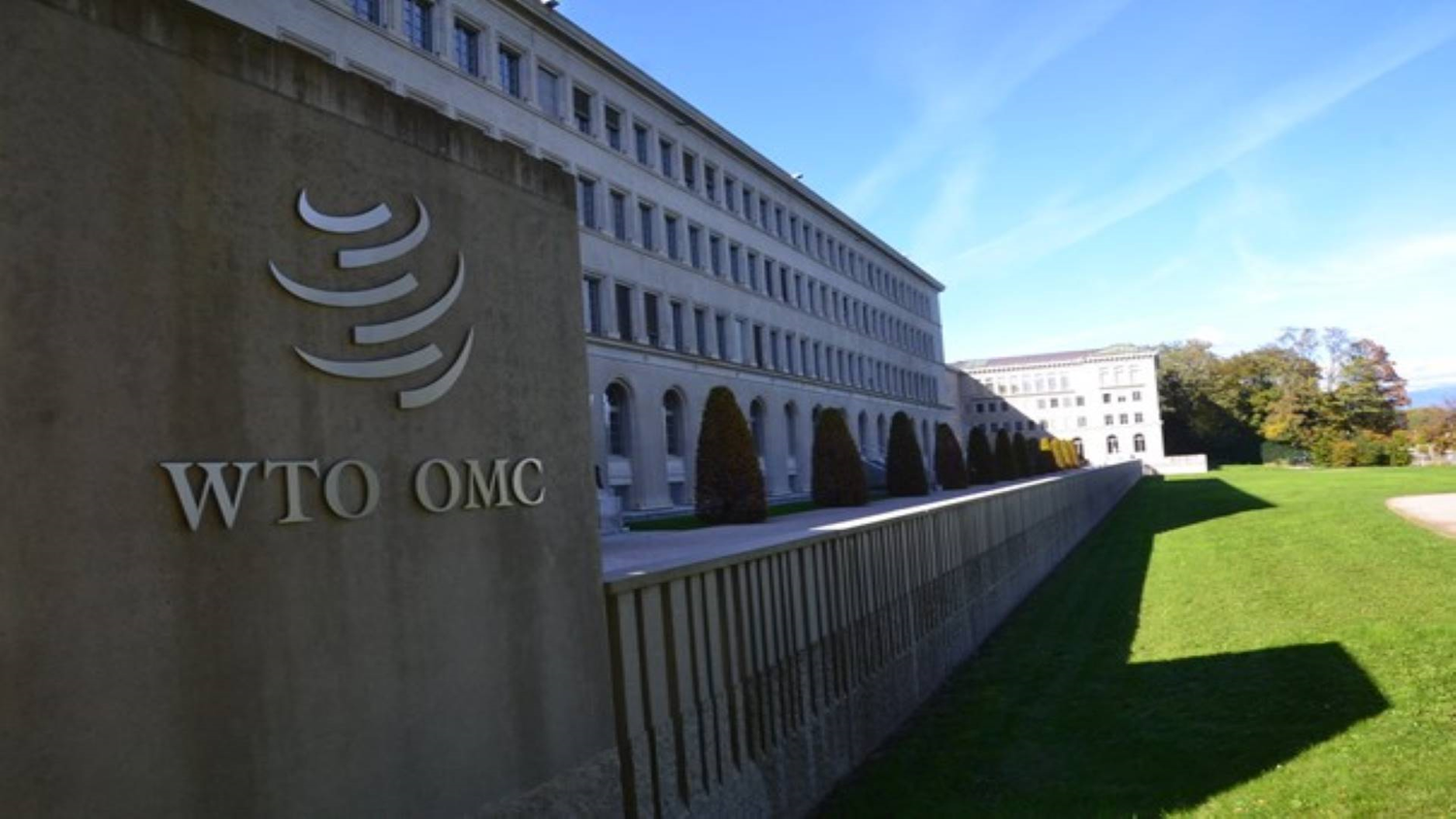 Un edificio lungo e un pannello con la scritta WTO OMC e il logo dell'Organizzazione mondiale del commercio in primo piano.