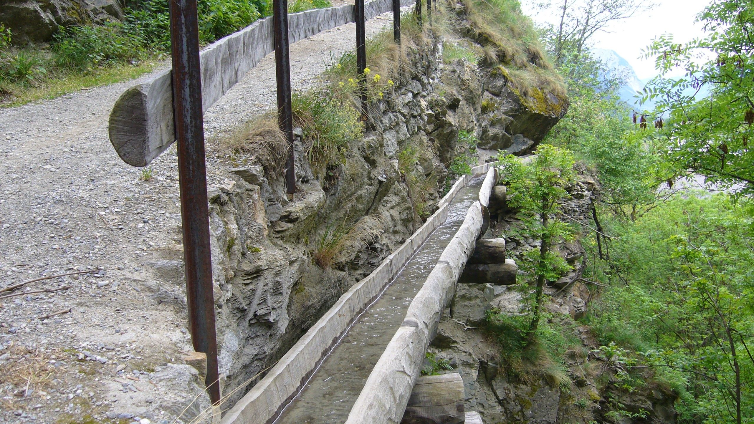 Suone in legno con acqua sotto una strada in ghiaia sul ripido fianco della montagna.